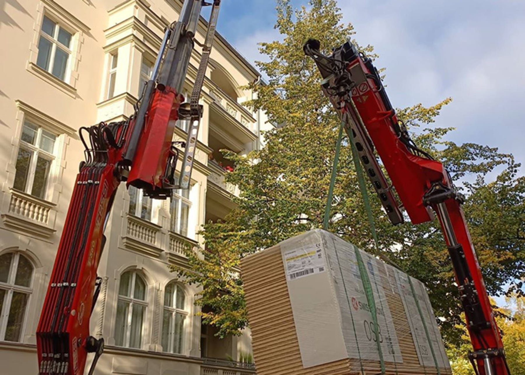 Kran hebt Holzbauelement vor Altbau-Fassade