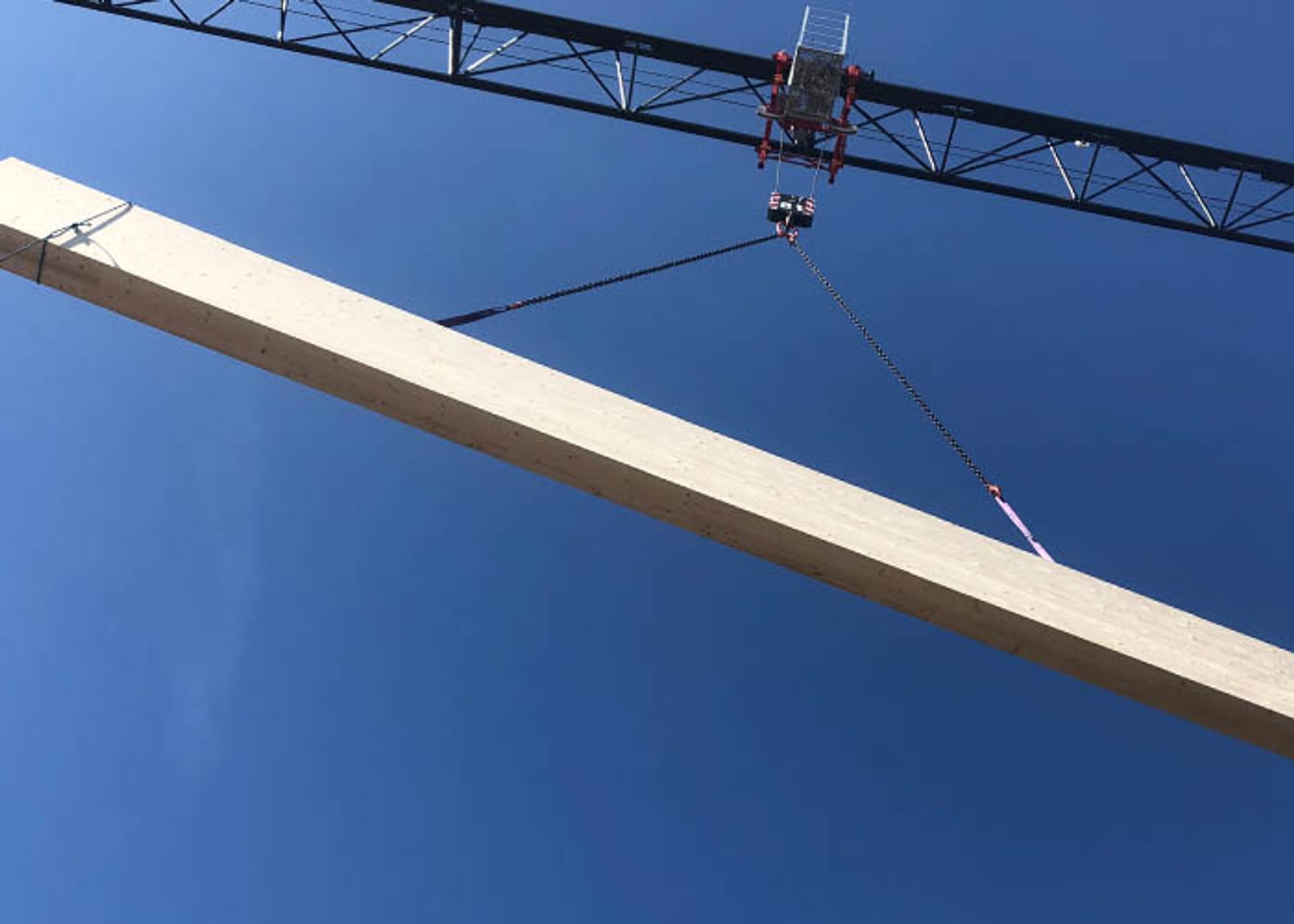 Holzbalken wird von Kran vor blauem Himmel gehoben